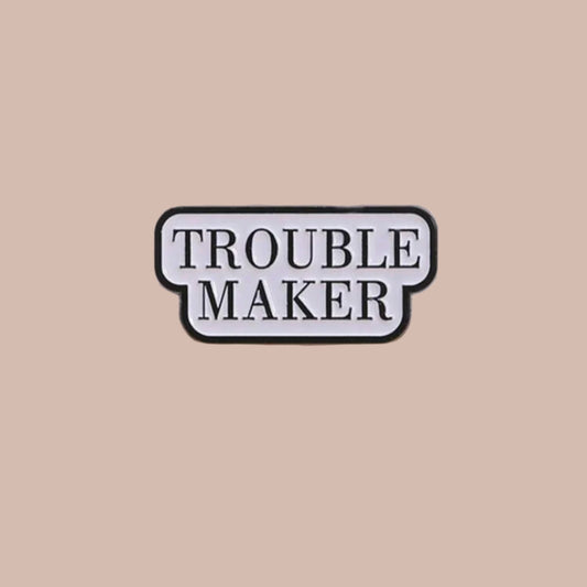 Enamel pin with 'TROUBLE MAKER' text on a plain background
